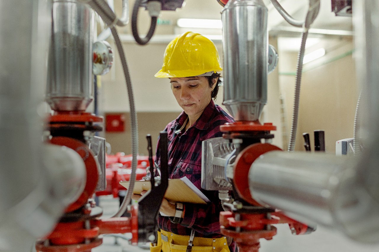 Female worker in hard hat inspecting the machinery and holding a clipboard