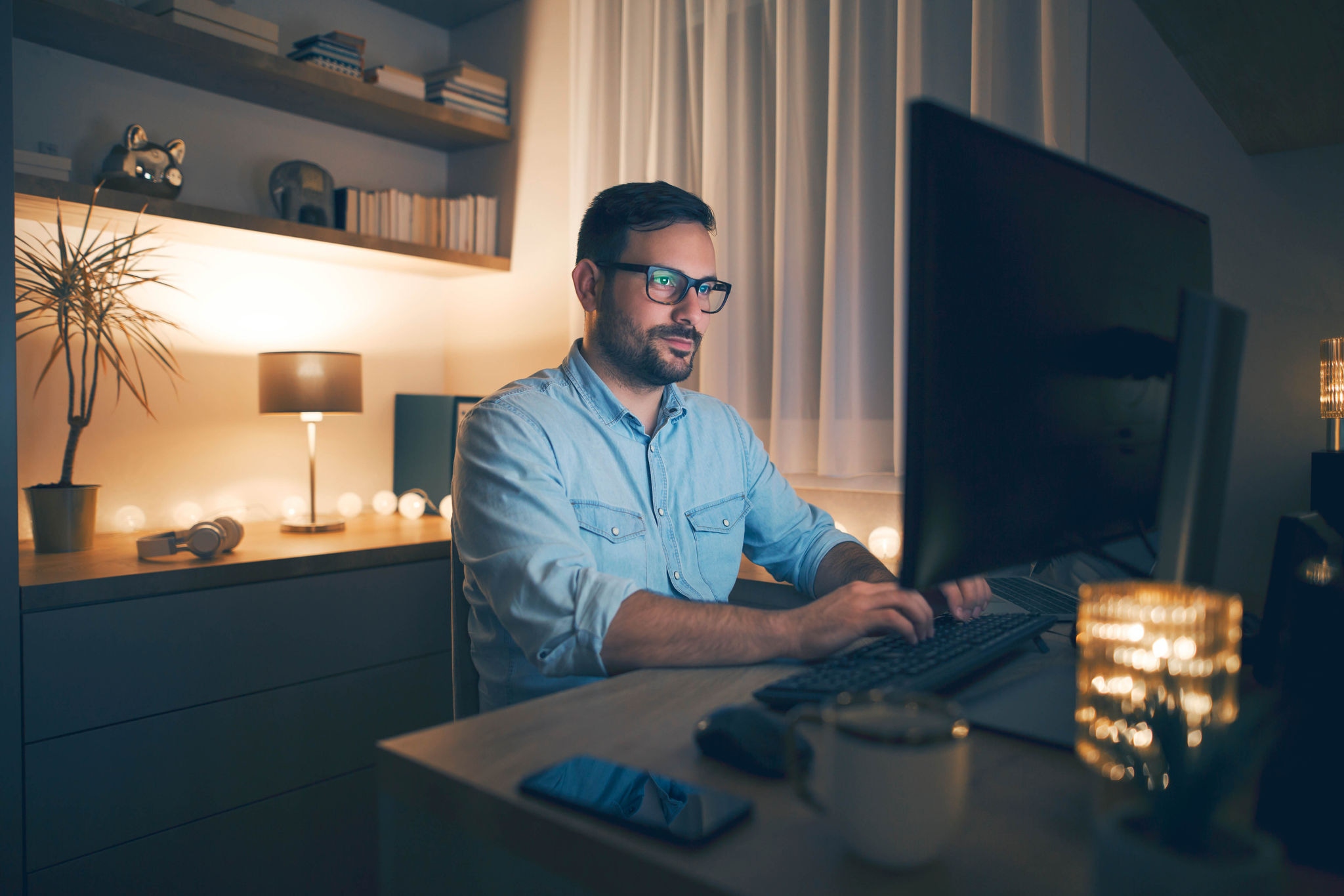 Man wearing a collared blue shirt typing on a computer