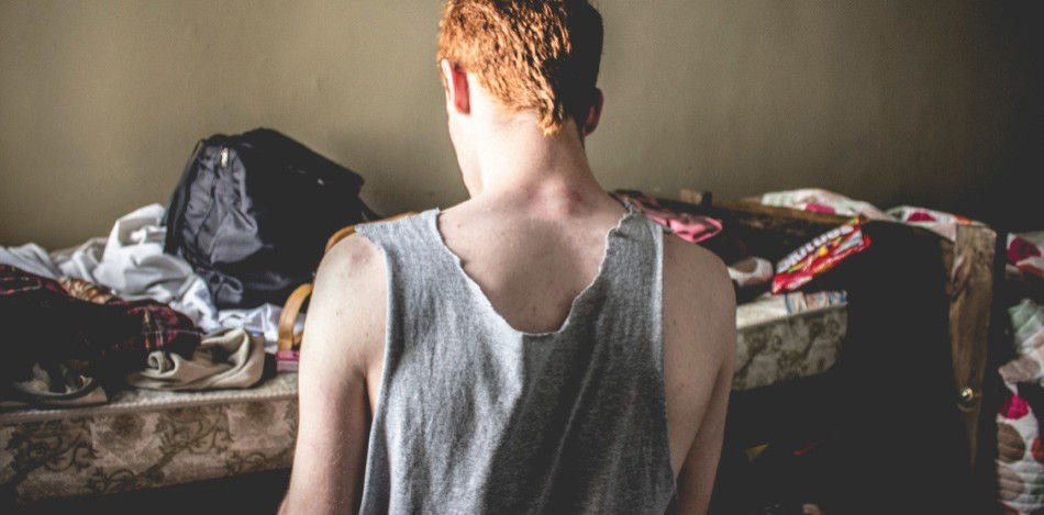 Red haired boy looking away from the camera at the mattress that has clothes on it